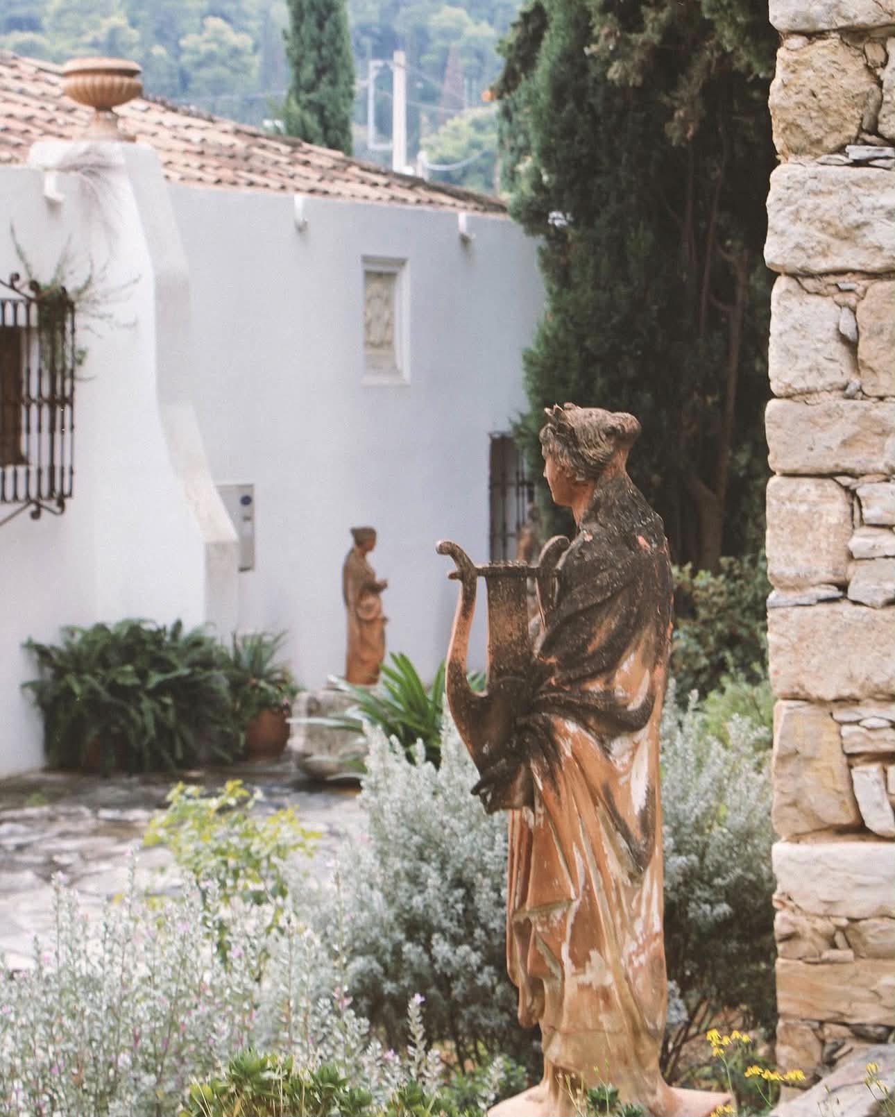 A statue holding a lyre among plants and stone walls in the museum garden